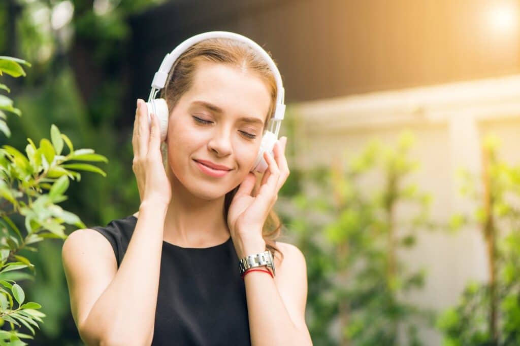 pexels-photo-1001850 Smiling woman listening to music with headphones in sunny garden setting.