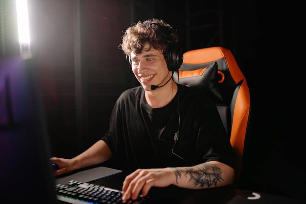 pexels-photo-9072296 A smiling young man enjoys PC gaming on a computer with headset in an indoor dark setting.